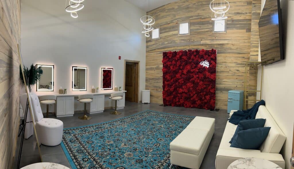Modern bridal suite at Round Mountain Cider Mill in Texas with vanity mirrors, white seating, a red rose photo wall, and teal accent rug