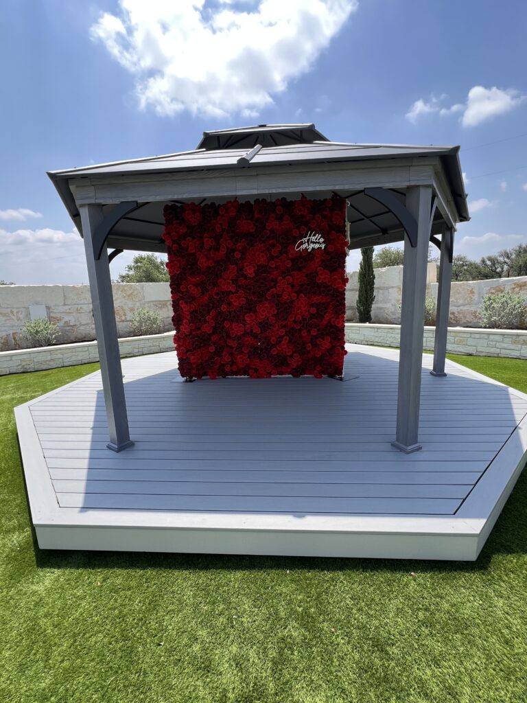 Gray gazebo on artificial turf at Round Mountain Cider Mill in Texas featuring a red rose backdrop wall with “Hello Gorgeous” sign