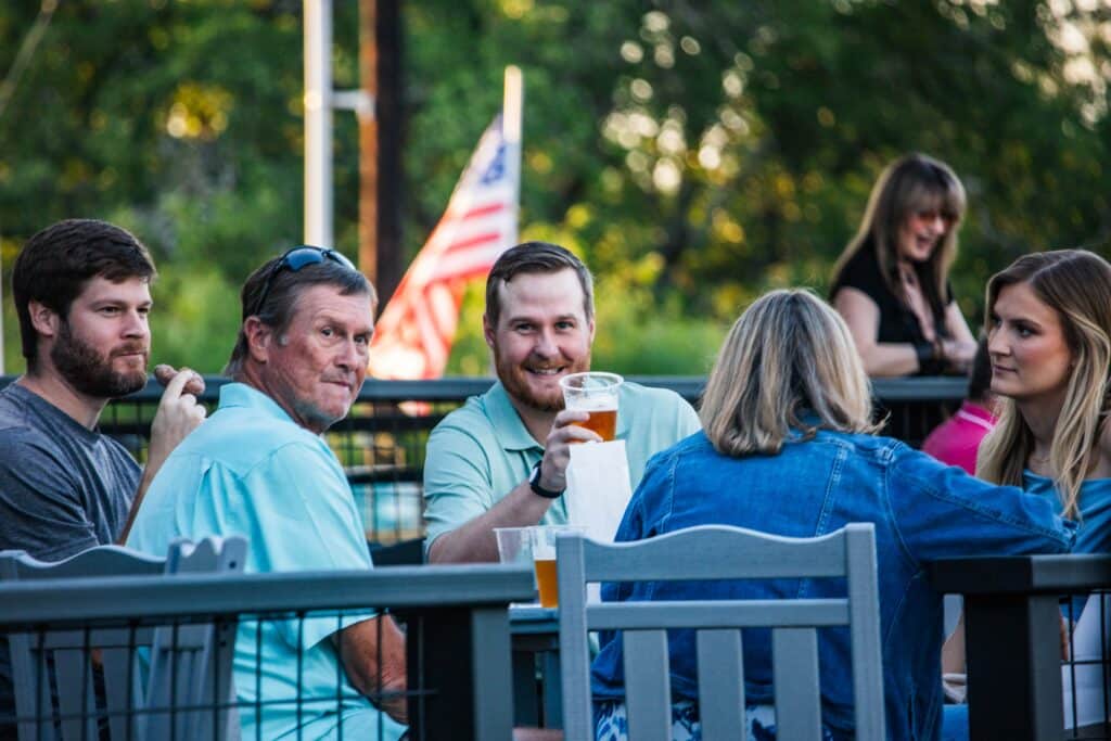 Group of guests enjoying cider and donuts outdoors at Round Mountain Cider Mill in Texas, with American flag in background