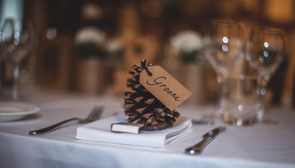 A beautifully arranged wedding table featuring a pine cone with a 'Groom' tag, adding rustic charm.